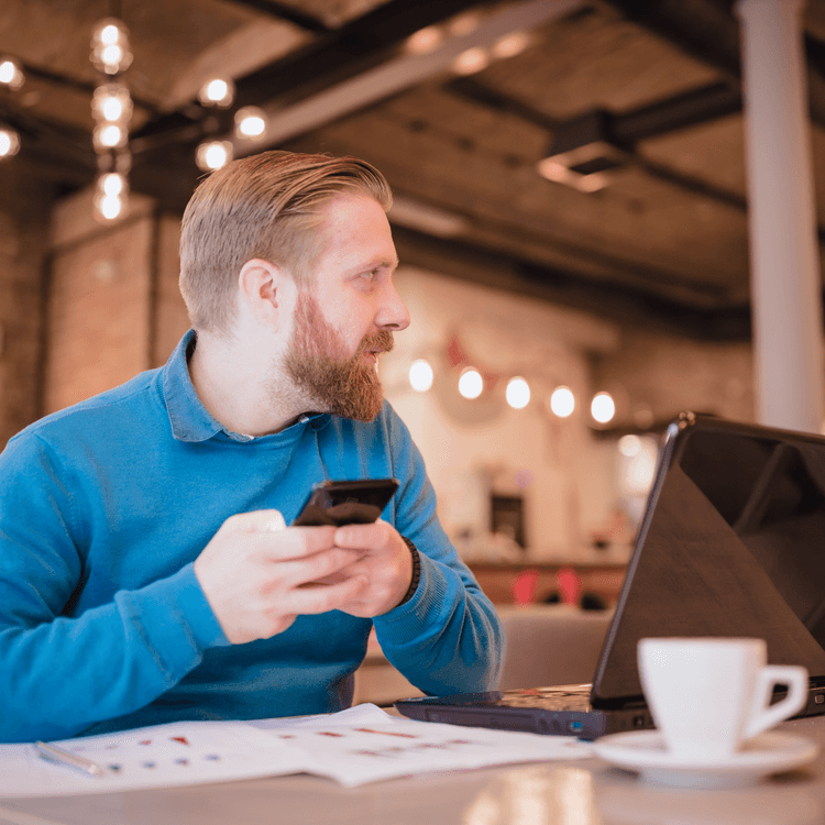 Man working on his laptop, with his mobile phone in his hands