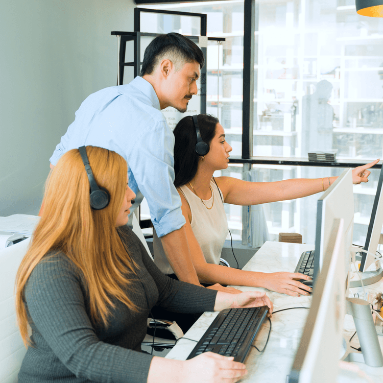 Two women working at a desk, with a man standing over them